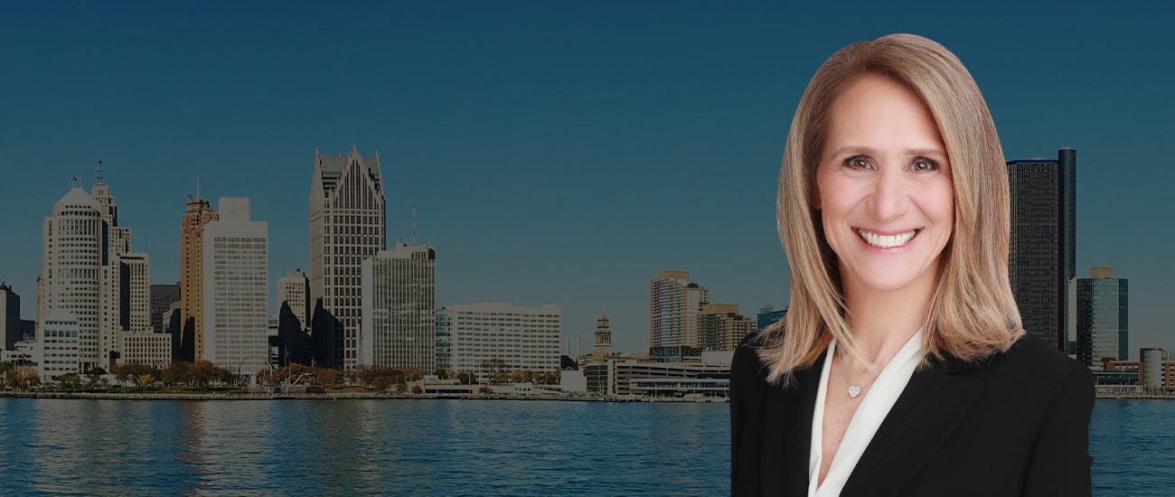 Ellen Michaels smiling in a black business suit, superimposed on a panoramic background of a city skyline with skyscrapers beside a calm body of water under a clear sky.